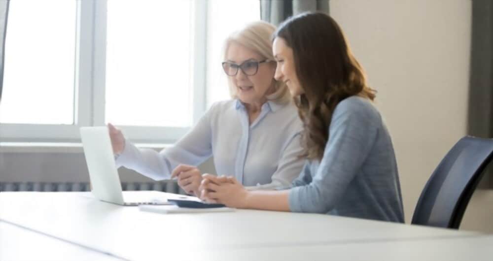 Illustrative photograph of two people discussing information beside a laptop